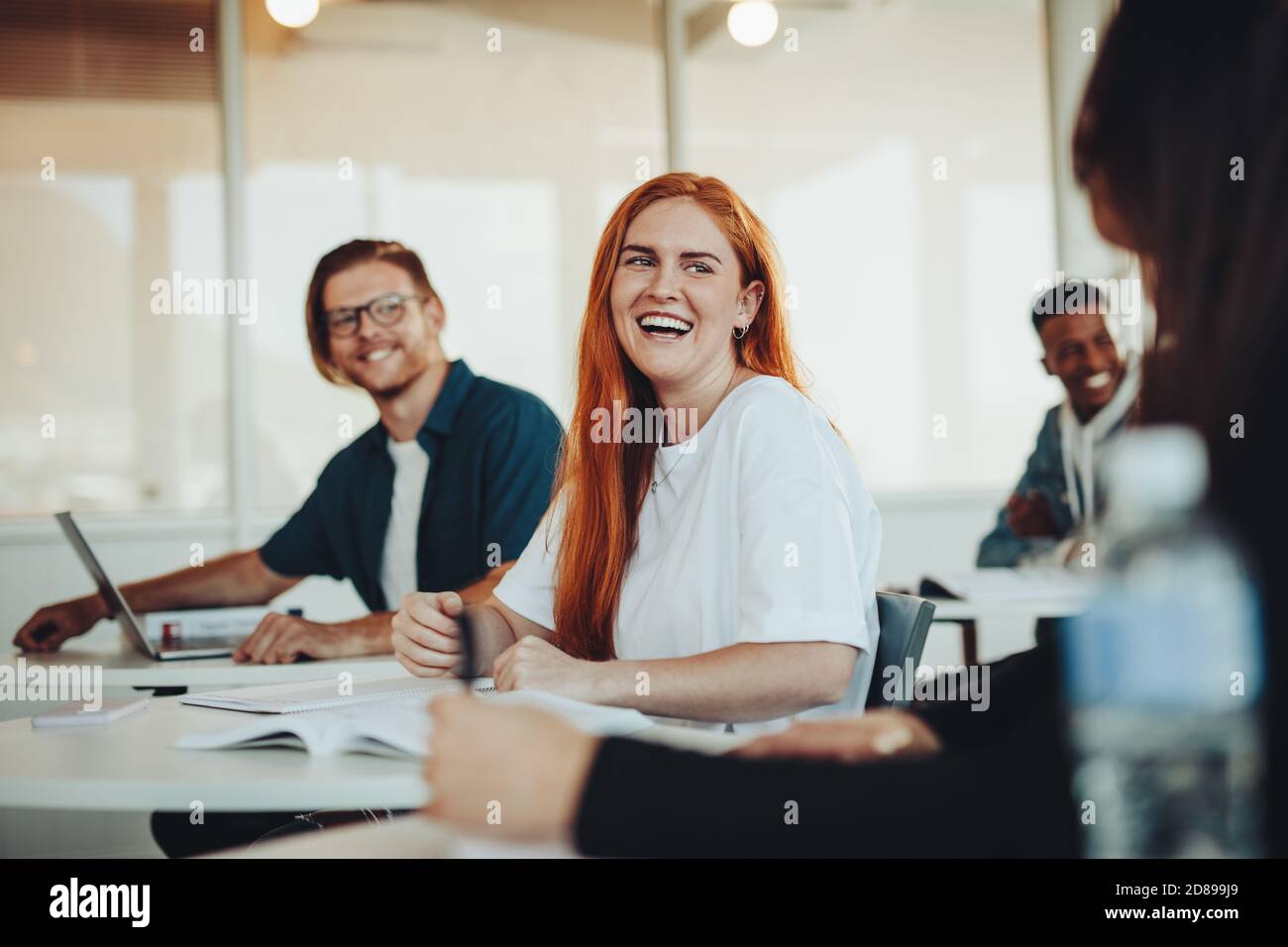 Smiling girl talking with classmates in classroom. Students chatting between the lectures in high school classroom. Stock Photo
