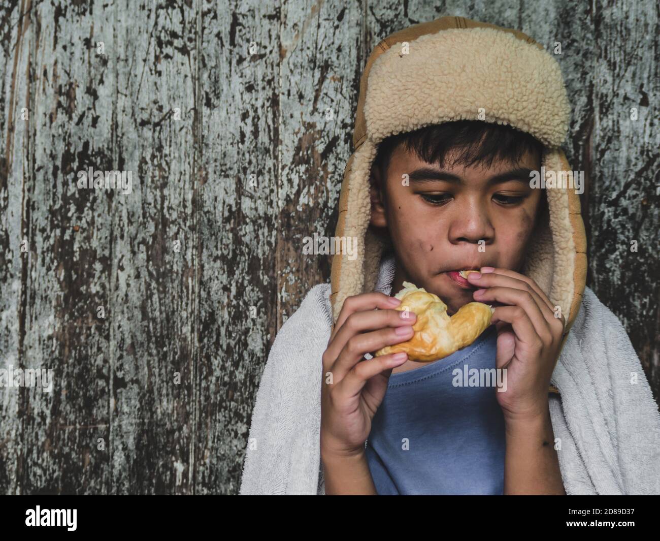 Hungry child eating bread that asking help for food donation from the people on street at the city. Unidentified homeless child begging on street. She Stock Photo