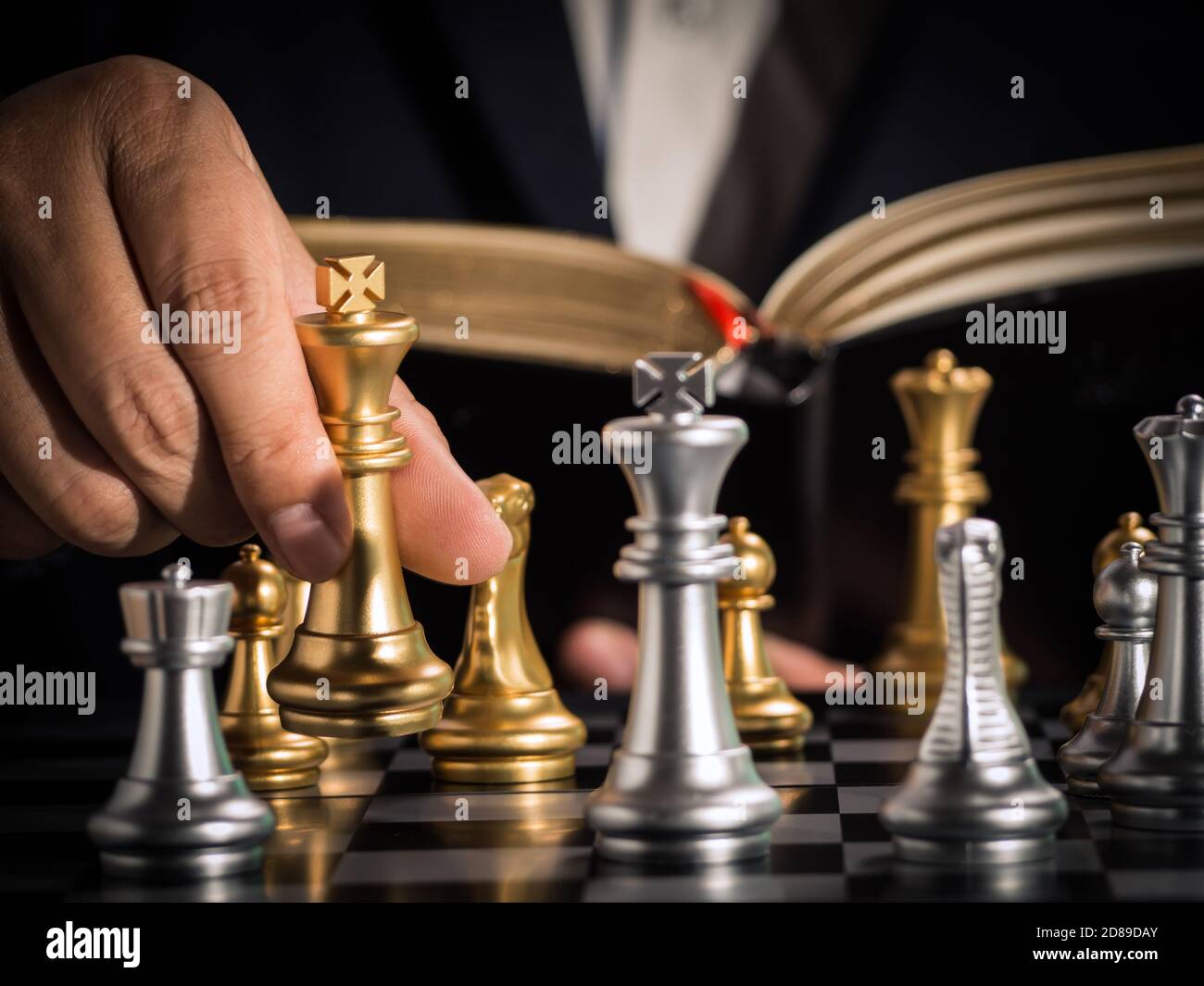 Hand of businessman moving the golden king chess to fighting silver king chess with opening book guideline play successfully in the competition. manag Stock Photo