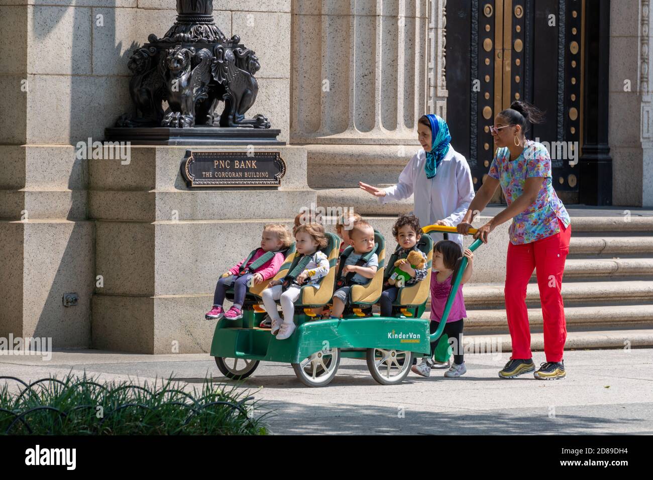 A group of young children in a KinderVan being pushed past the former PNC Bank Corcoran Building in Pennsylvania Avenue, Washington DC Stock Photo