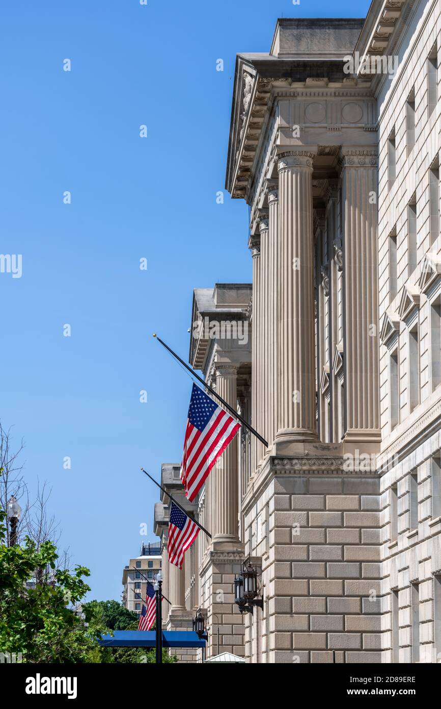 US flags fly at half-staff from the four neoclassical pedimented pavilions of the Herbert C Hoover Building on 15th Street NW, Washington DC Stock Photo