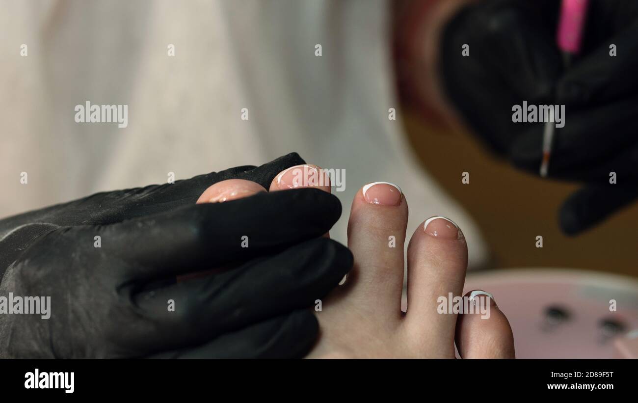 Process pedicure close up in a fashionable spa salon, unrecognizable people. French pedicure, white gel polish Stock Photo