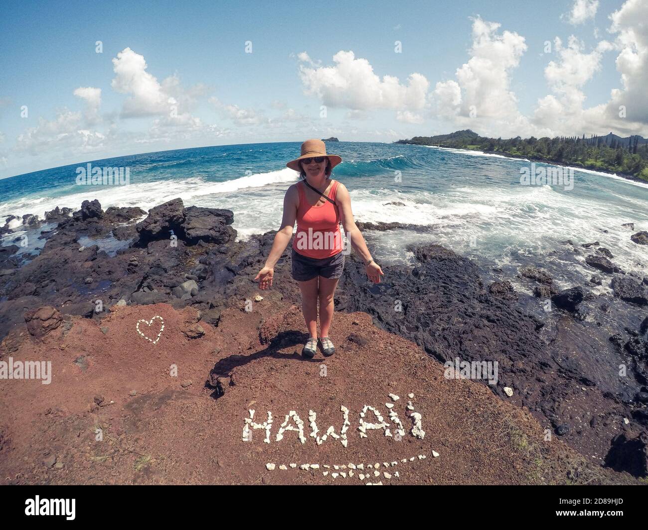 Smiling woman standing by ocean with rocks spelling word Hawaii, Hawaii, USA Stock Photo