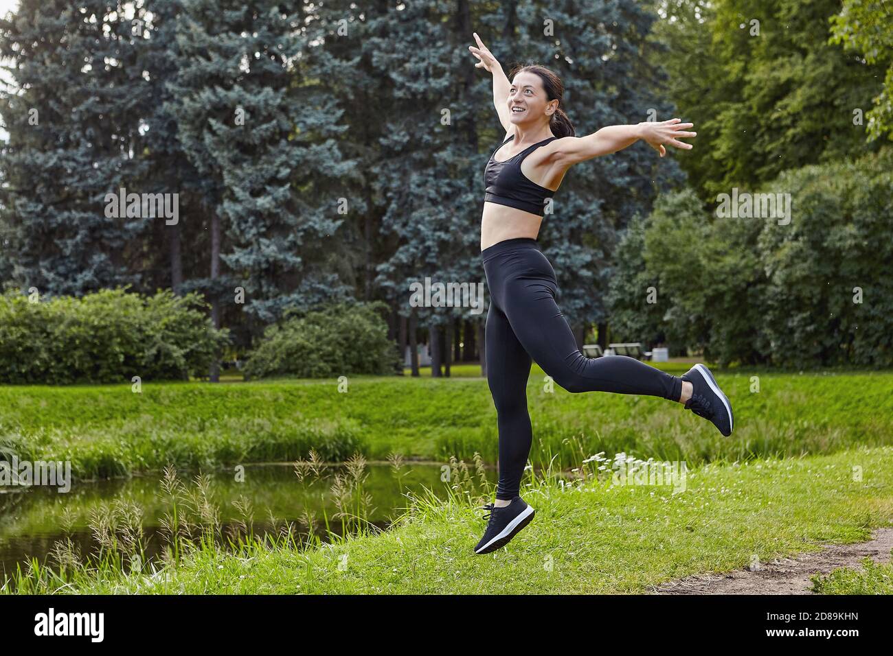 Slim woman makes yoga near pond outdoors. Stock Photo