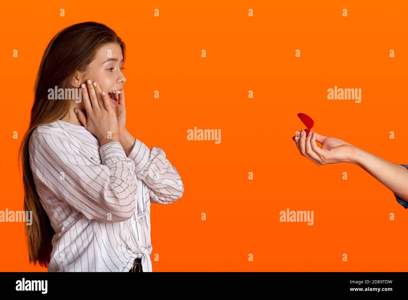 Marry me. Happy surprised young woman press her hands to cheeks and screams with joy and looks at males hand Stock Photo