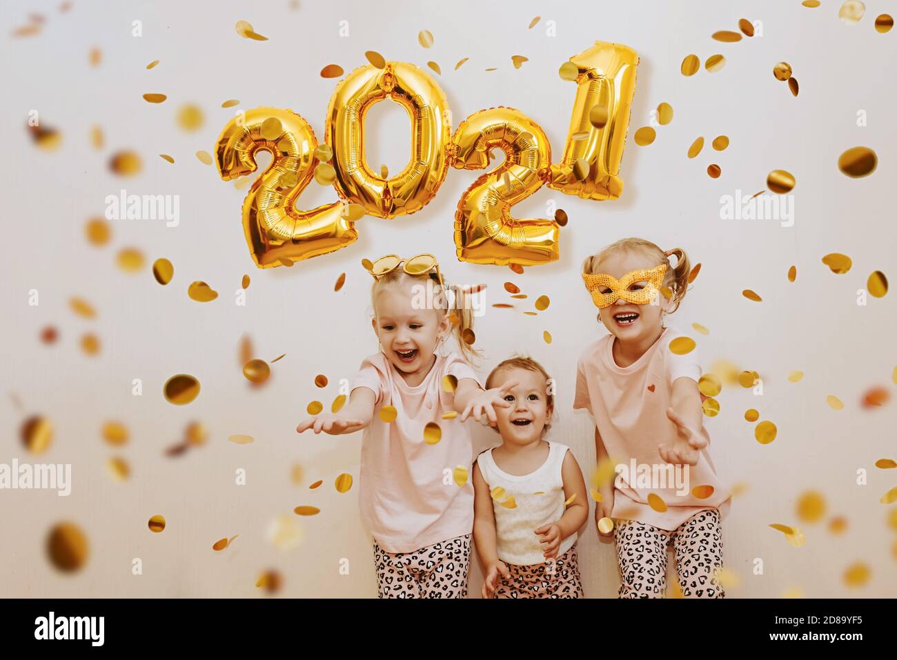 Three little girls are enjoying the flying golden confetti. Celebrating 2021 Stock Photo
