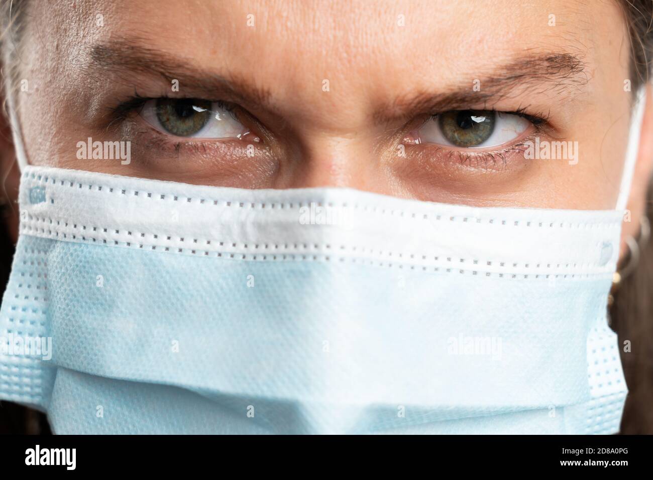 Close-up of adult woman eyes making angry expression wearing surgical or medical disposable mask to prevent covid19 infection isolated on white studio Stock Photo