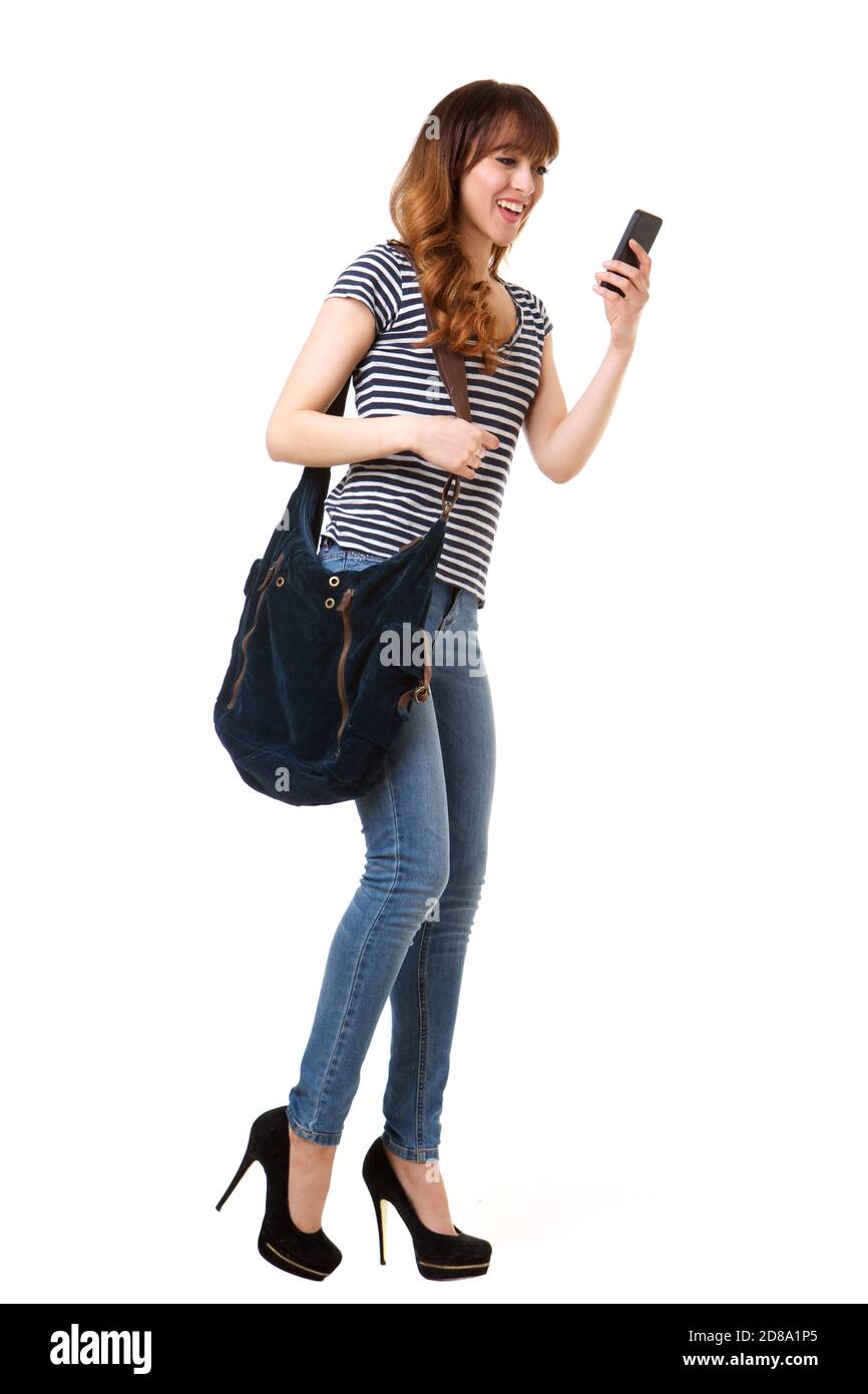 Full length portrait of happy young woman walking with mobile phone and purse against isolated white background Stock Photo