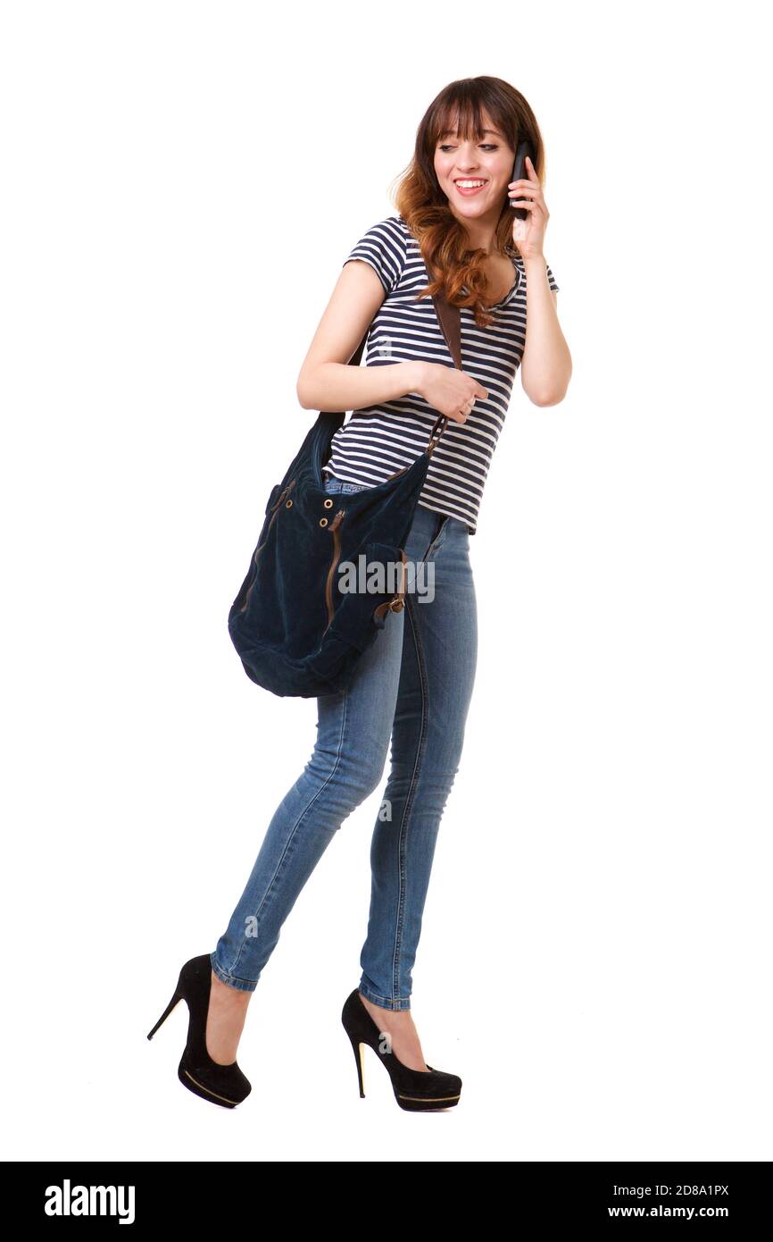 Full length portrait of young woman walking against white background with mobile phone and purse Stock Photo