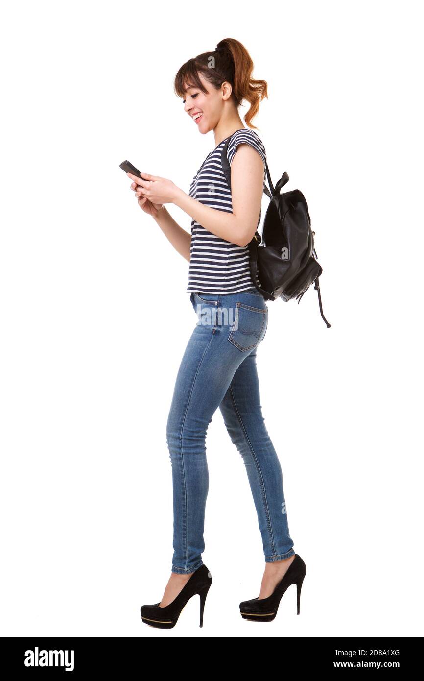 Full length side portrait of young woman walking with mobile phone and bag against white background Stock Photo