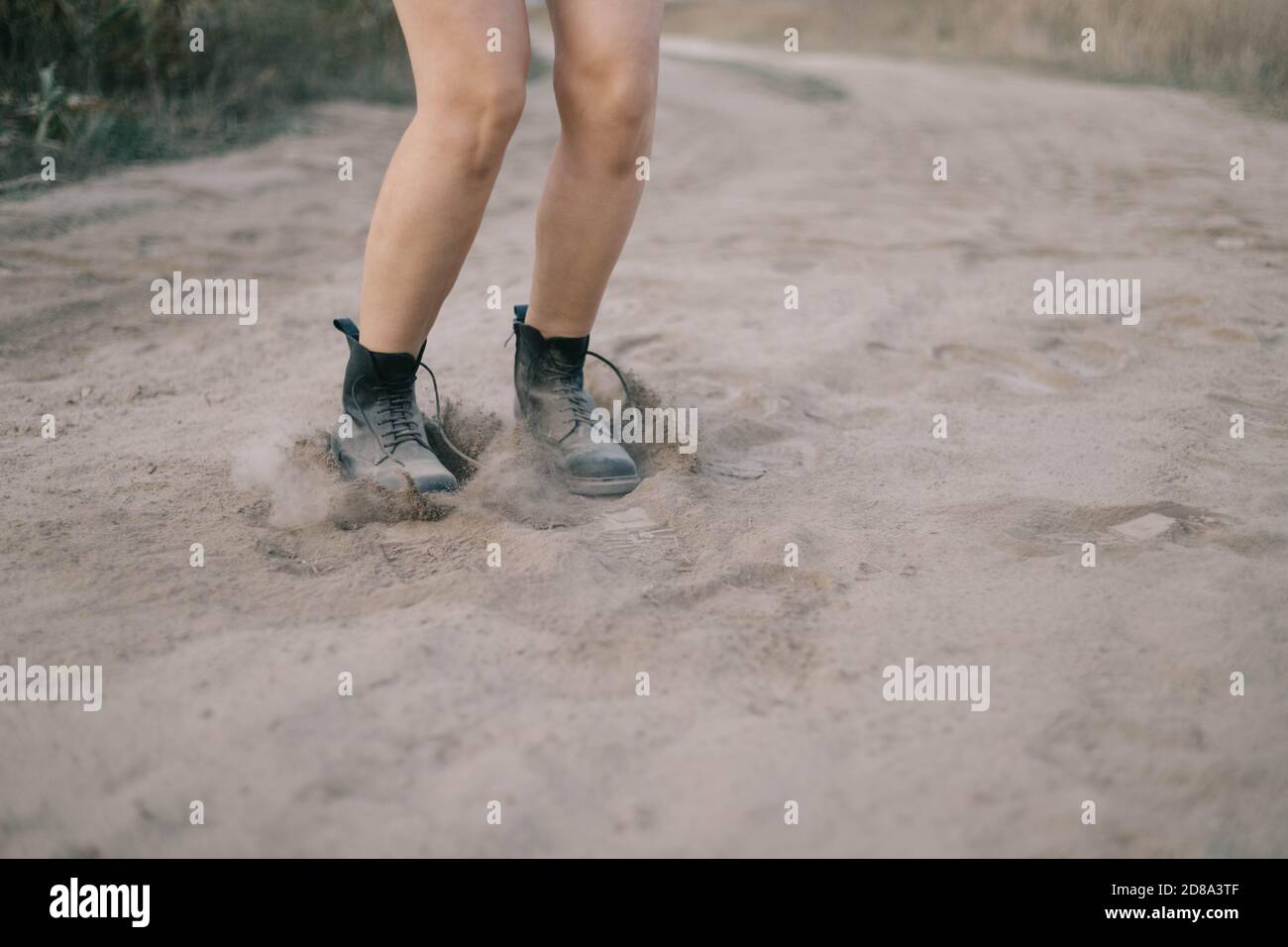 female legs jumping in the desert through fine dust carrying clouds of