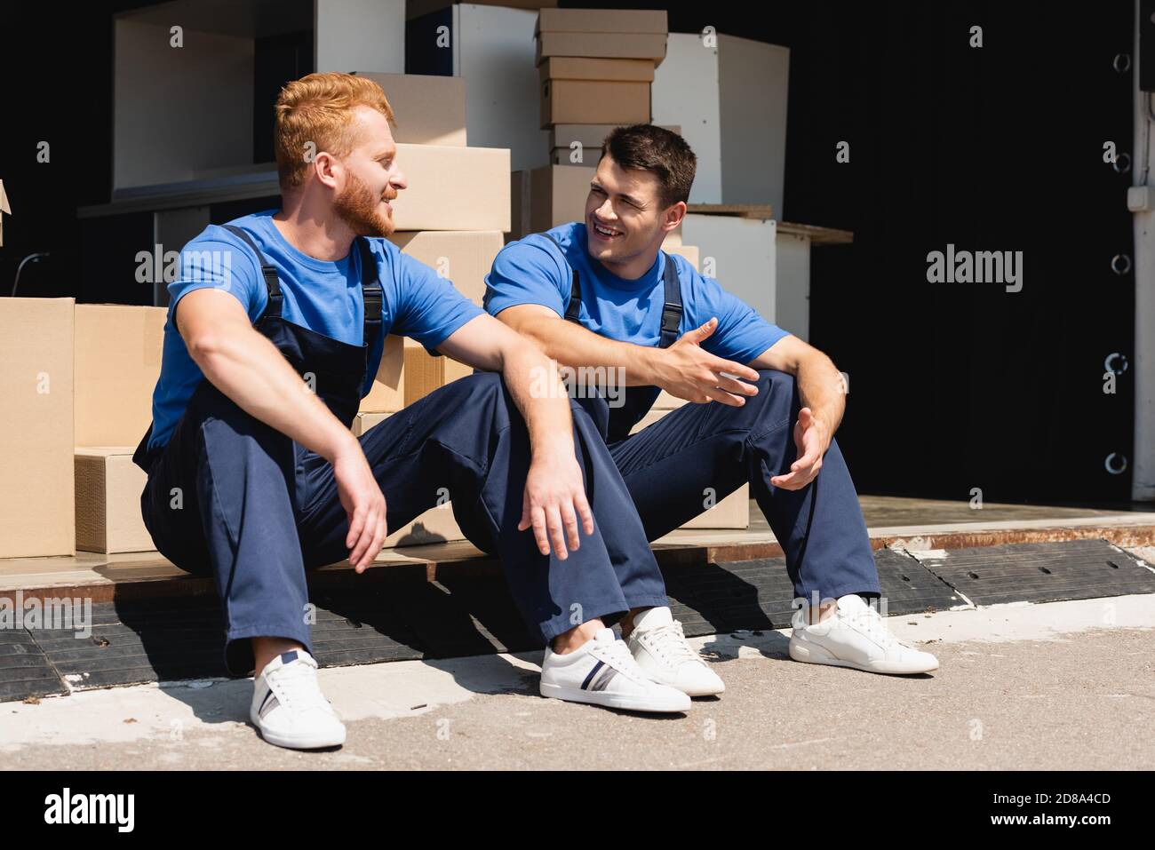 Movers talking while sitting in warehouse outdoors Stock Photo
