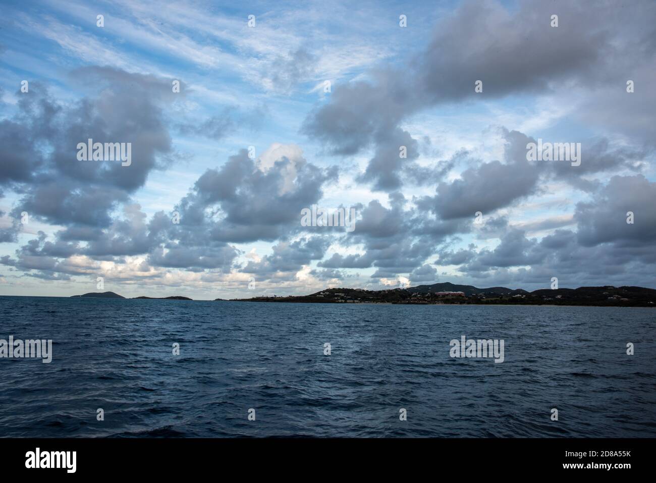 View from the Caribbean Sea into the rolling landscape of St. Croix at dusk under a cloudy sky. Stock Photo