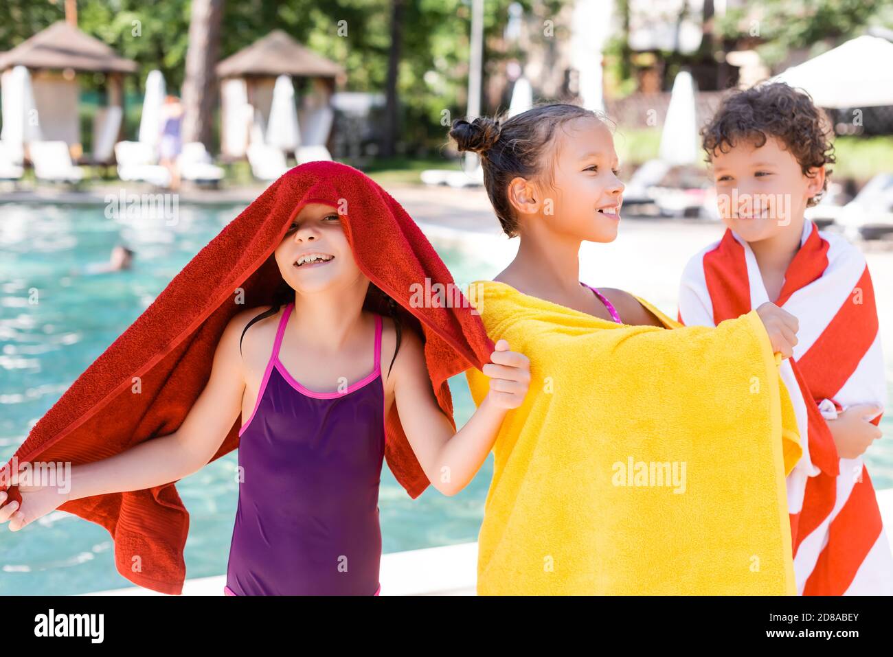 excited girl in swimsuit covering head with towel while standing near