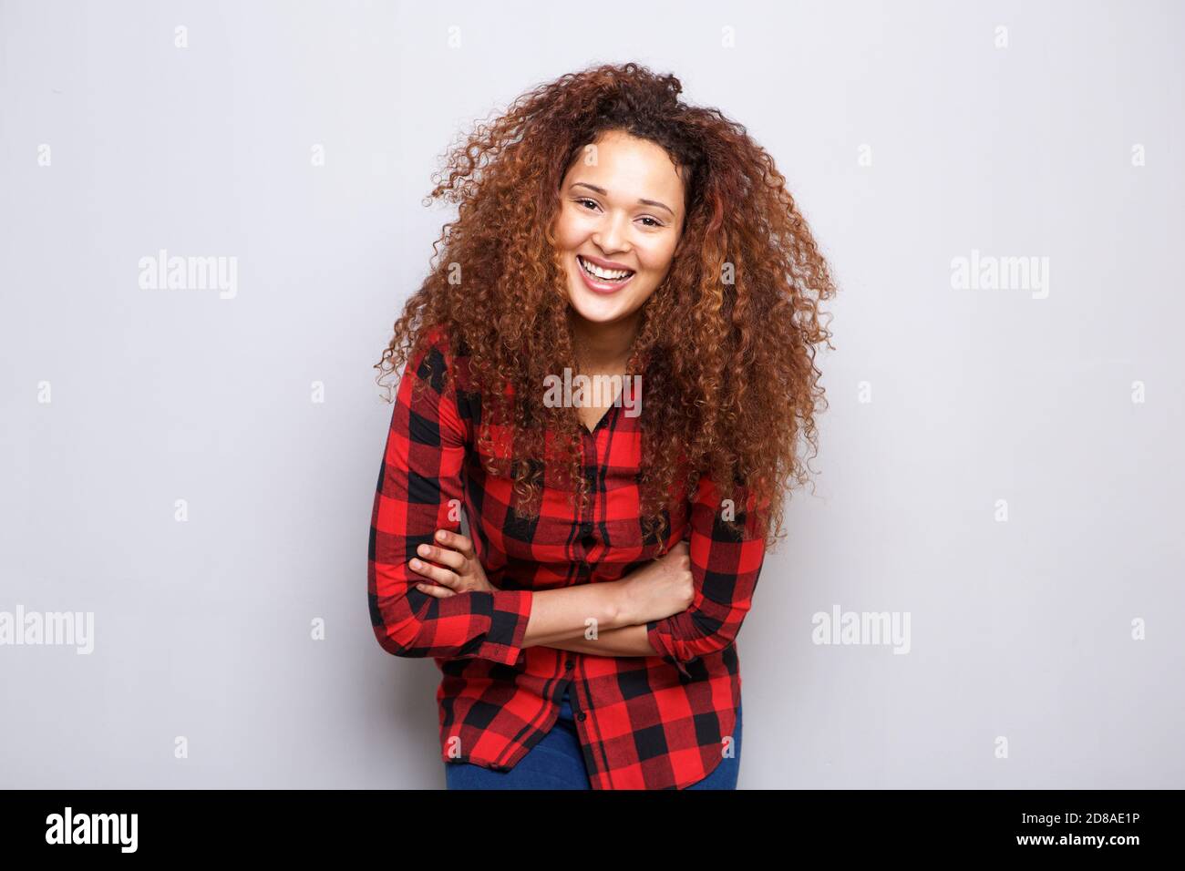 Portrait of happy young woman with curly hair smiling against gray ...