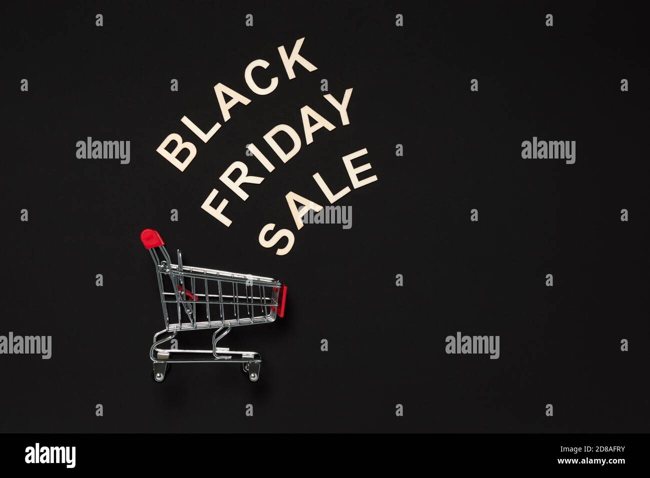 Black Friday sale word made with wooden letters above red shopping cart on dark background. Shopping, commerce and sale concept. Flat lay banner with Stock Photo