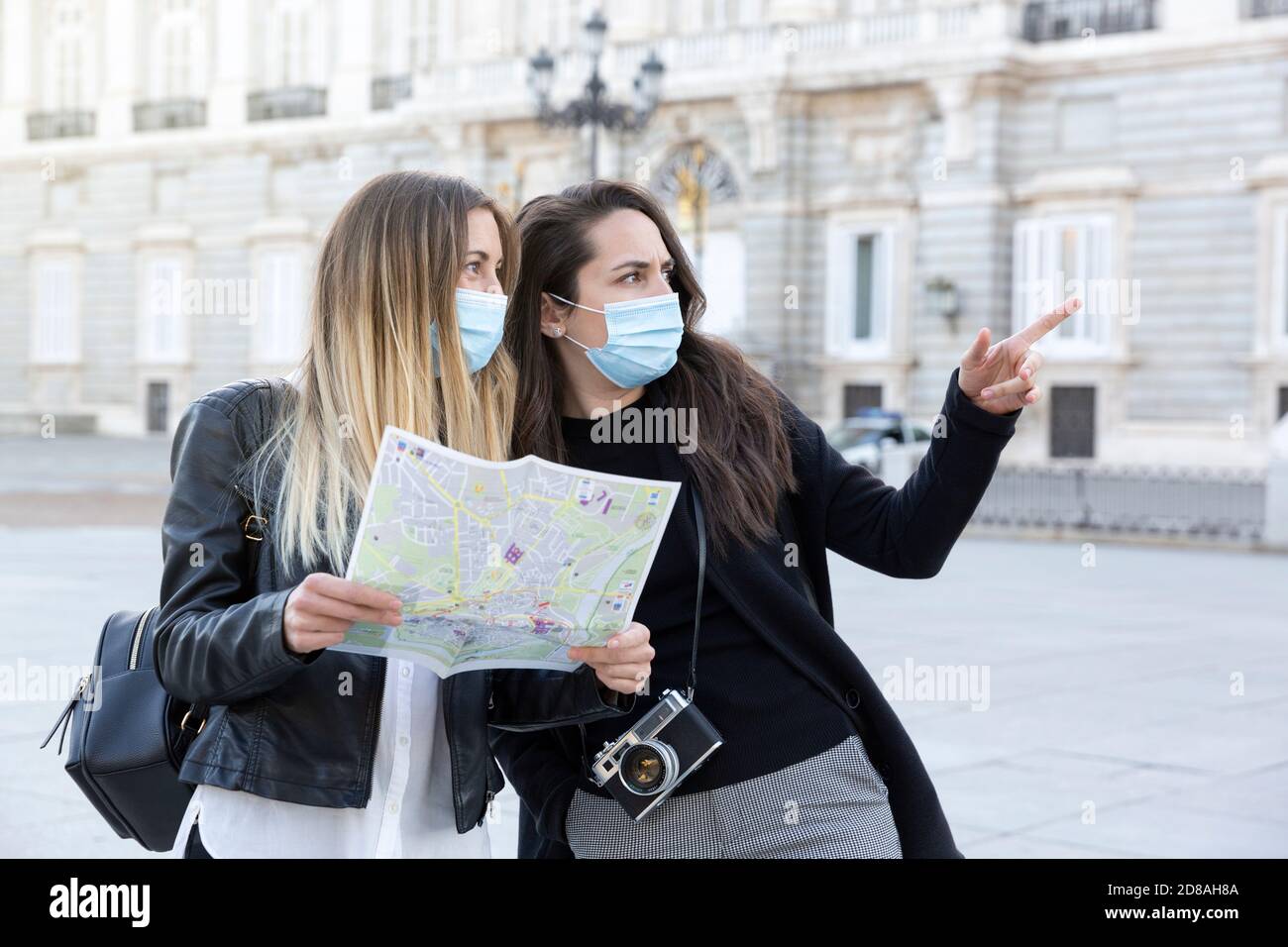 Two girls traveling together in the city. They have a tourist map and are wearing medical masks. Concept of travel and new normal. Stock Photo