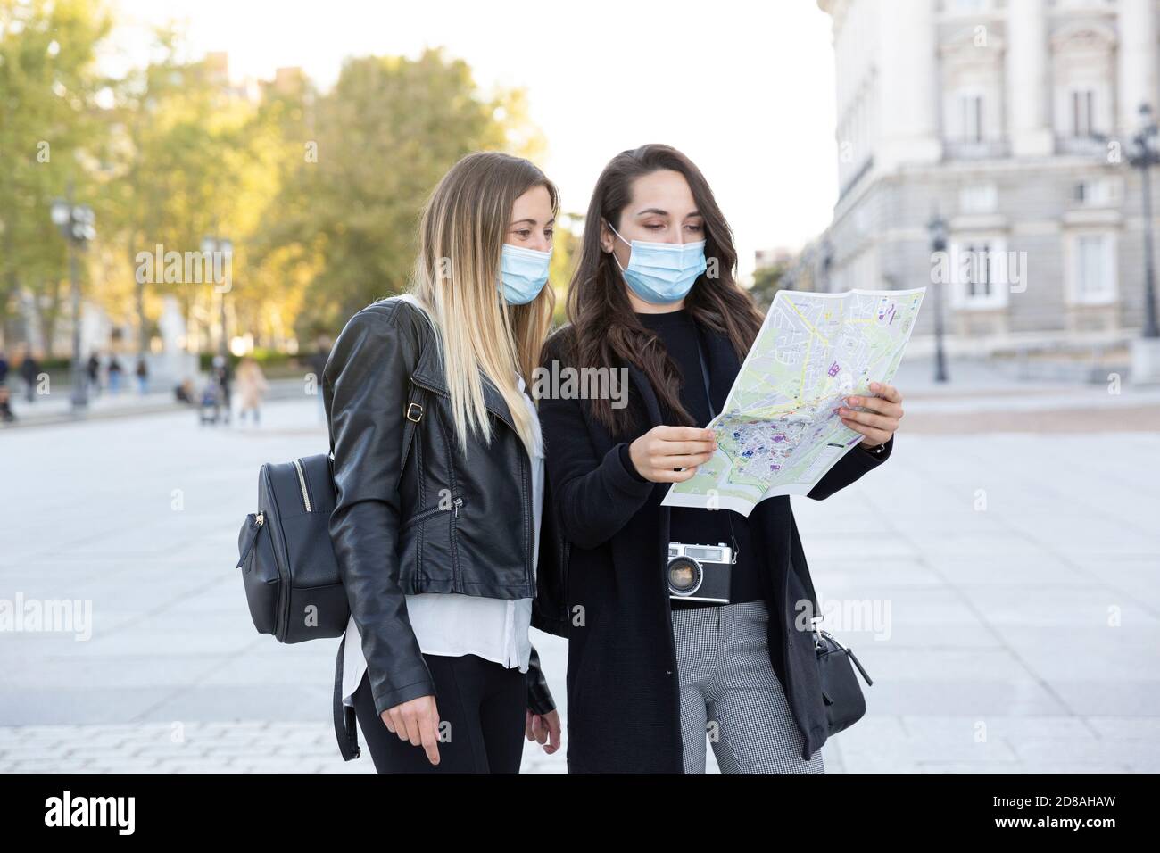 Two girl friends standing in the city looking at a tourist map. They are wearing face masks. Concept of new normal. Stock Photo