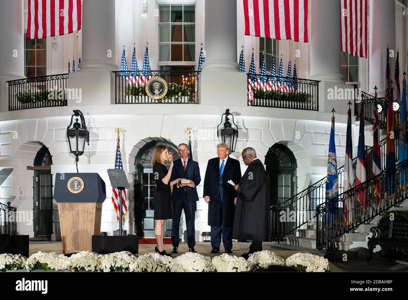 President Donald J. Trump looks on as U.S. Supreme Court Associate Justice Clarence Thomas swears in Judge Amy Coney Barrett to be the Supreme Court's 115th associate justice Monday, Oct. 23, 2020, on the South Lawn of the White House in Washington, D.C. Justice Barrett is joined by her husband Jesse, holding the Bible, and their children. (USA) Stock Photo