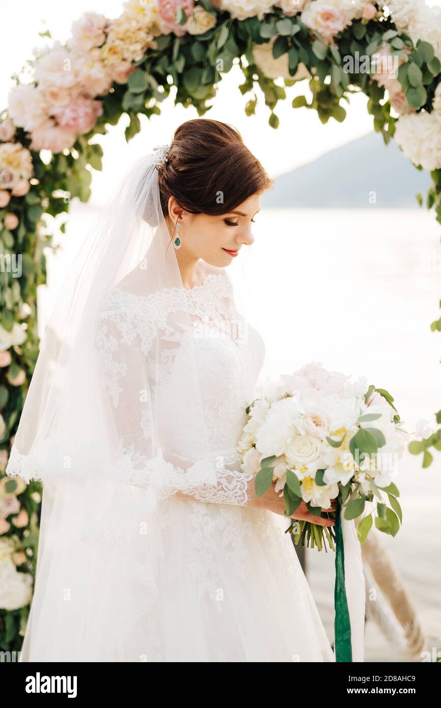 beautiful bride with a veil and bridal bouquet near the wedding arch ...