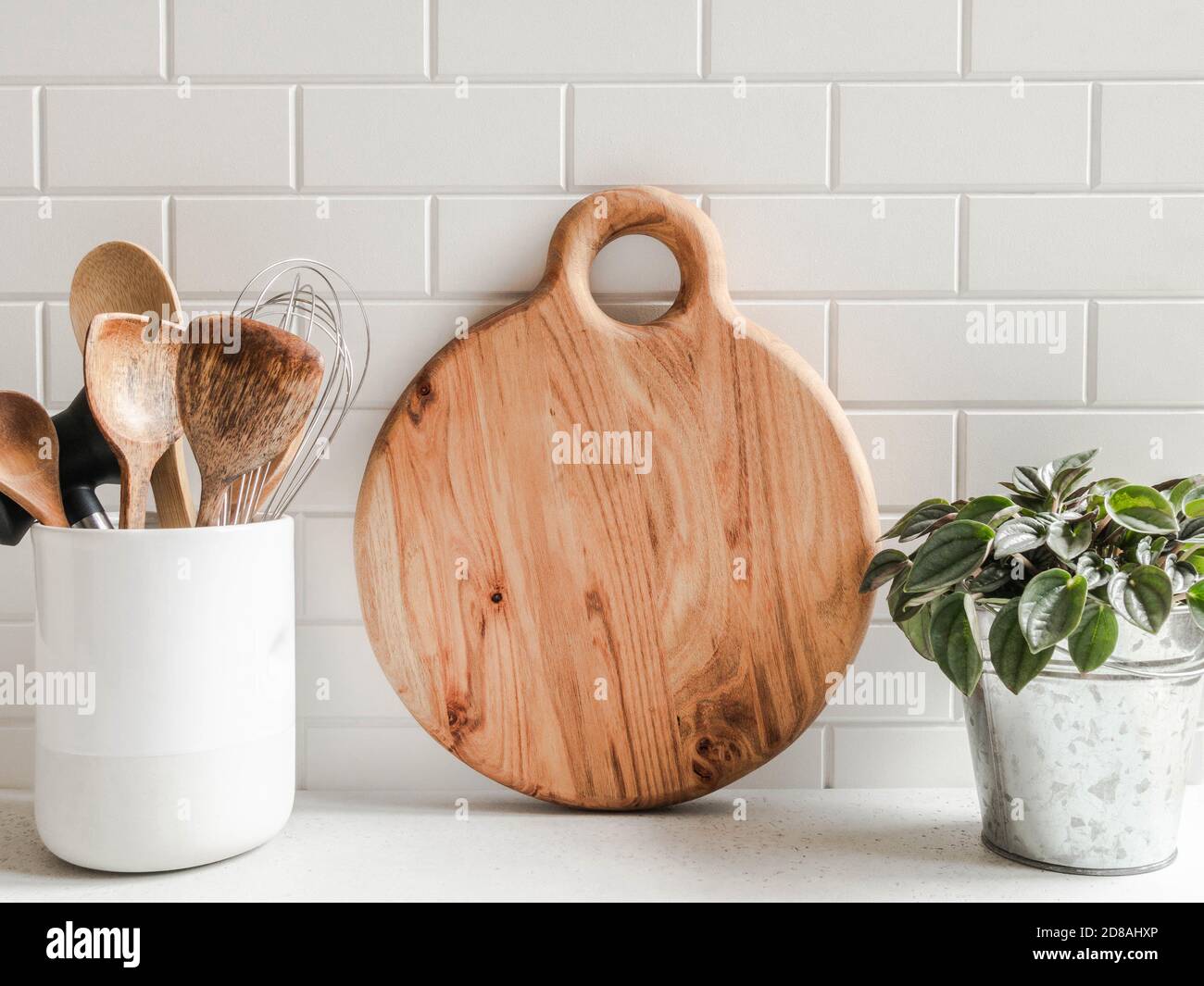 Stylish white kitchen background with kitchen utensils and wood cutting board for text on white countertop, copy space, front view Stock Photo