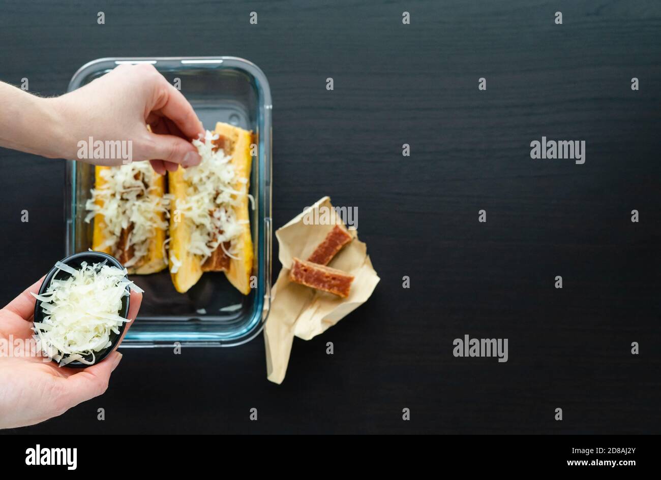 Hand putting cheese to cook Ripe banana in the oven with guava and cheese sandwich on a black wooden base. Typical Colombian food concept. Copy space. Stock Photo