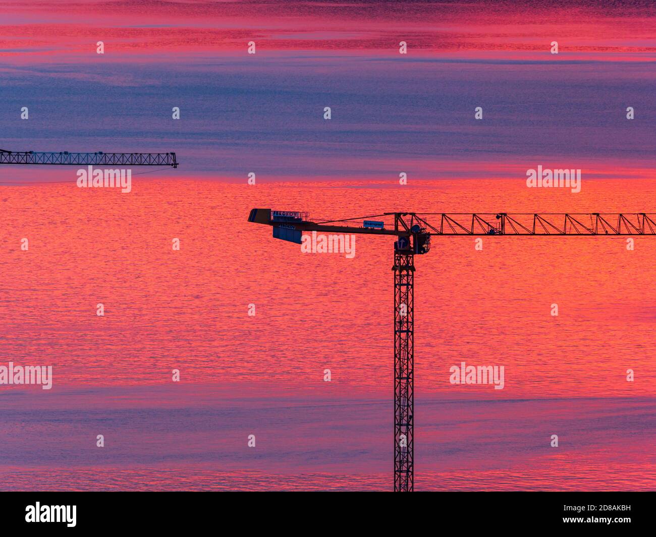 Real estate building crane against sunset evening dusk warm color sea calm surface reflection, Rijeka in Croatia Europe Stock Photo