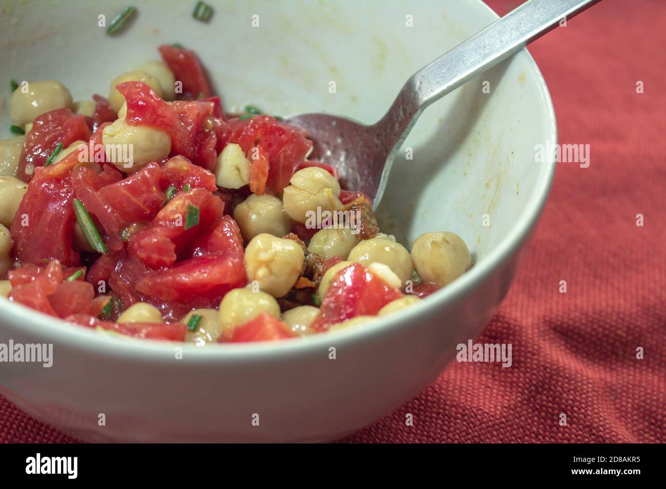 Detail on a white bowl with a chickpea, tomato and rosemary salad inside Stock Photo