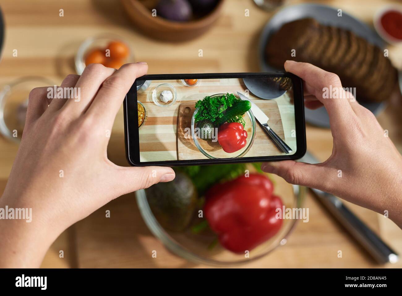Close-up of female hands holding mobile phone and making photo of fresh vegetables in bowl Stock Photo