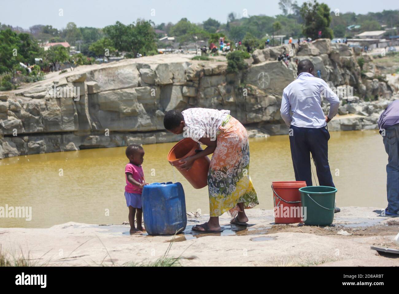A woman with her child fetches water from an unprotected dead pool. Despite the risk and dangers at the dead pool many residents still go and fetch water in dangerous area. Epworth is one of the areas without tap water. Zimbabwe. Stock Photo
