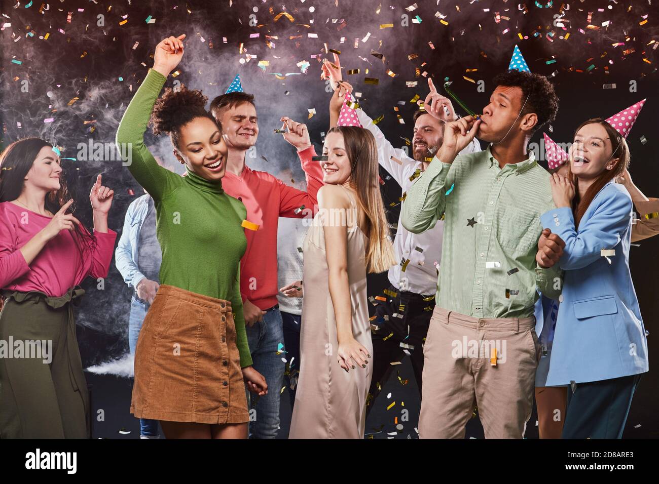 Celebrating holiday with friends. Group of young happy multiracial people dancing and having fun, confetti falling in the air Stock Photo