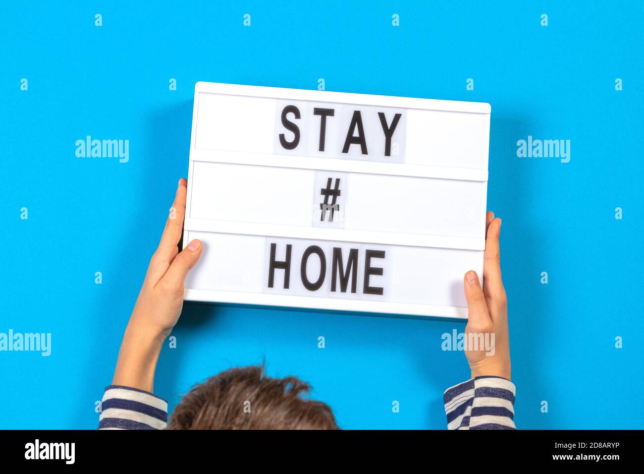 Kid hands holding white lightbox with text STAY HOME on blue background. Coronavirus, Covid-19, quarantines and Social distancing concept Stock Photo