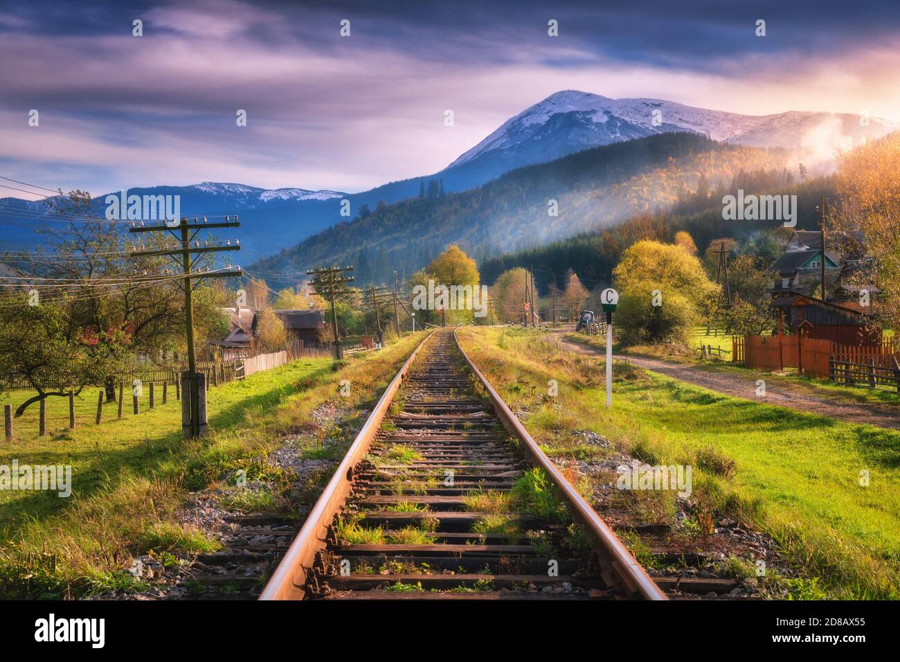Railroad in mountains with snowy peaks at sunset in autumn Stock Photo
