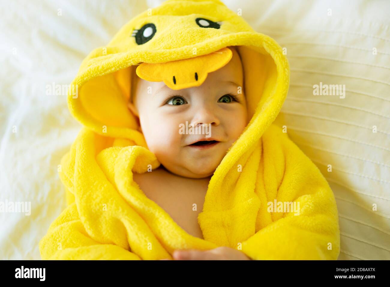 Baby wearing yellow bathrobe duck on parents bed after bath Stock Photo Alamy