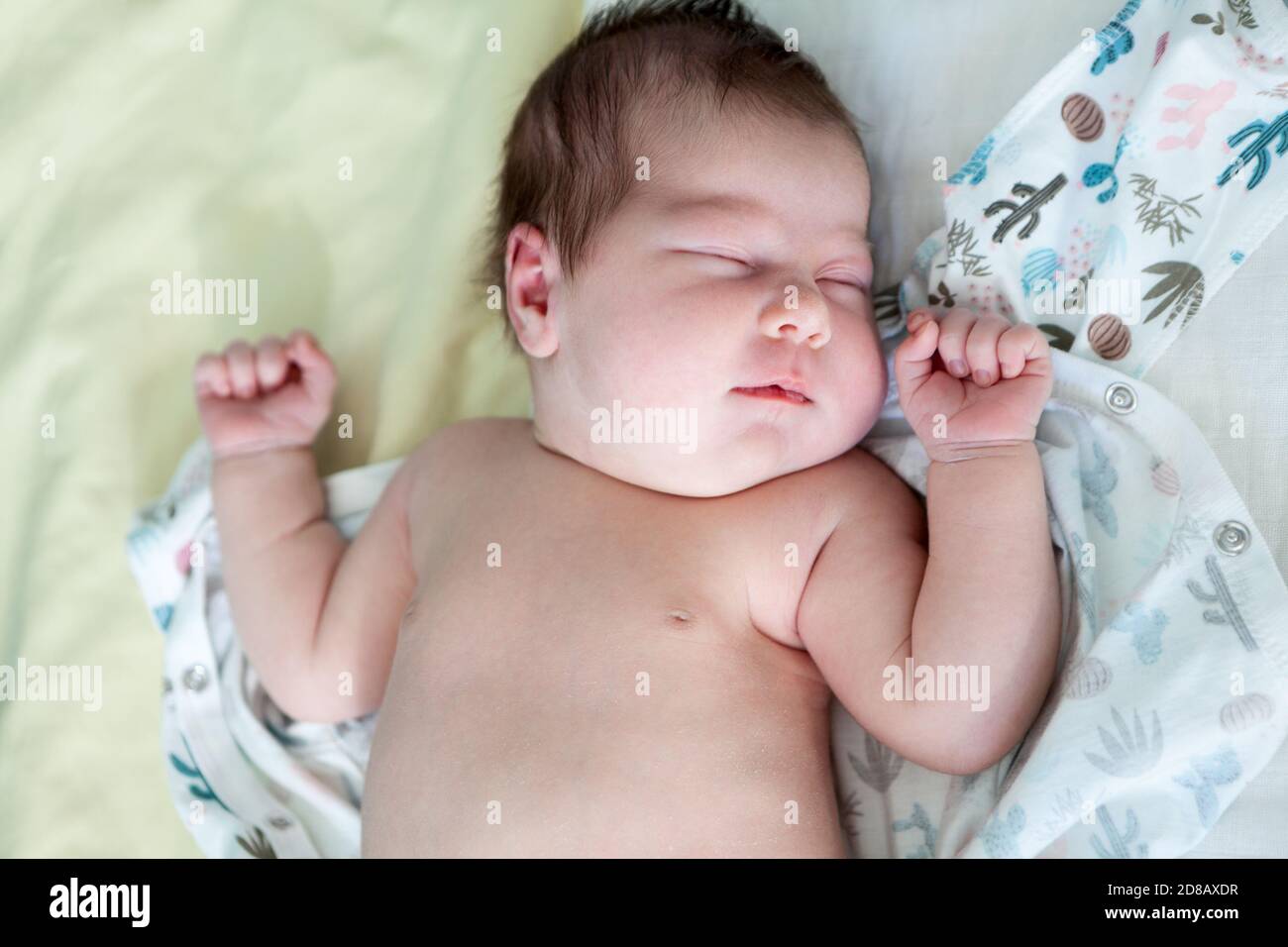 Adorable newborn baby sleeping with hands up, lying in bed Stock Photo