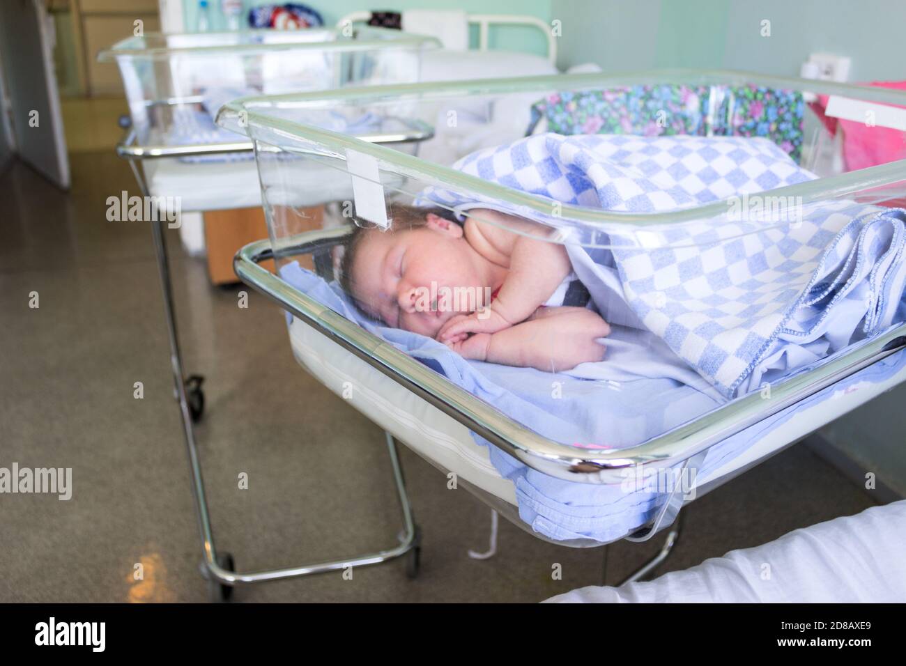 Cute little newborn baby sleeping in infant bed in hospital, folded hands with open mouth, under blanket Stock Photo