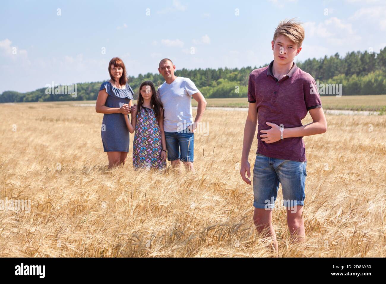 Concept of an adopted kid, boy standing on foreground with adoptive family on background, stepson with dad, mom and preteen sister Stock Photo