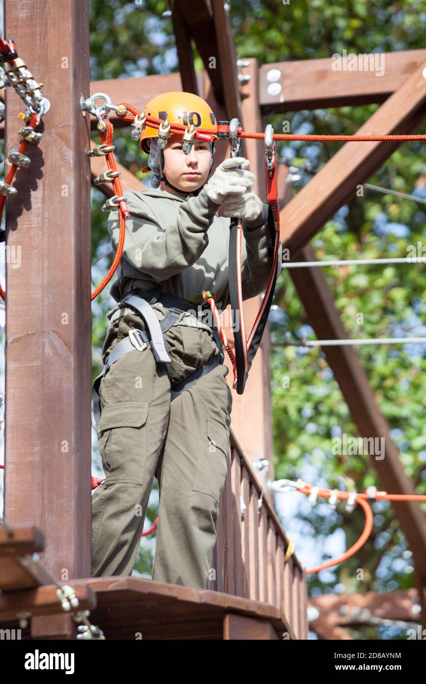 Preteen girl climbs on rope course wearing climbing equipment Stock Photo