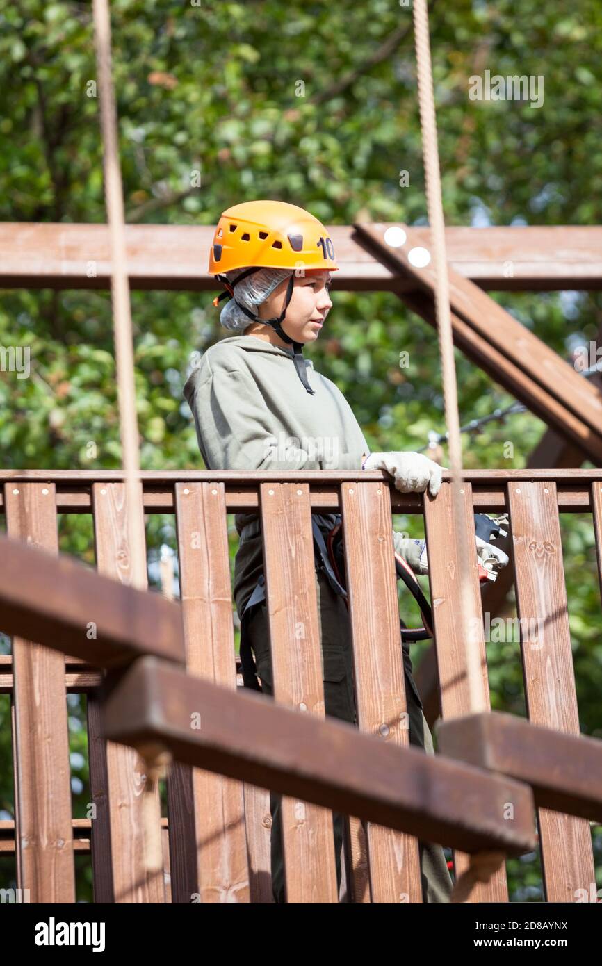 Pre-teen girl starting an obstacle course wearing climbing equipment, adventure park Stock Photo
