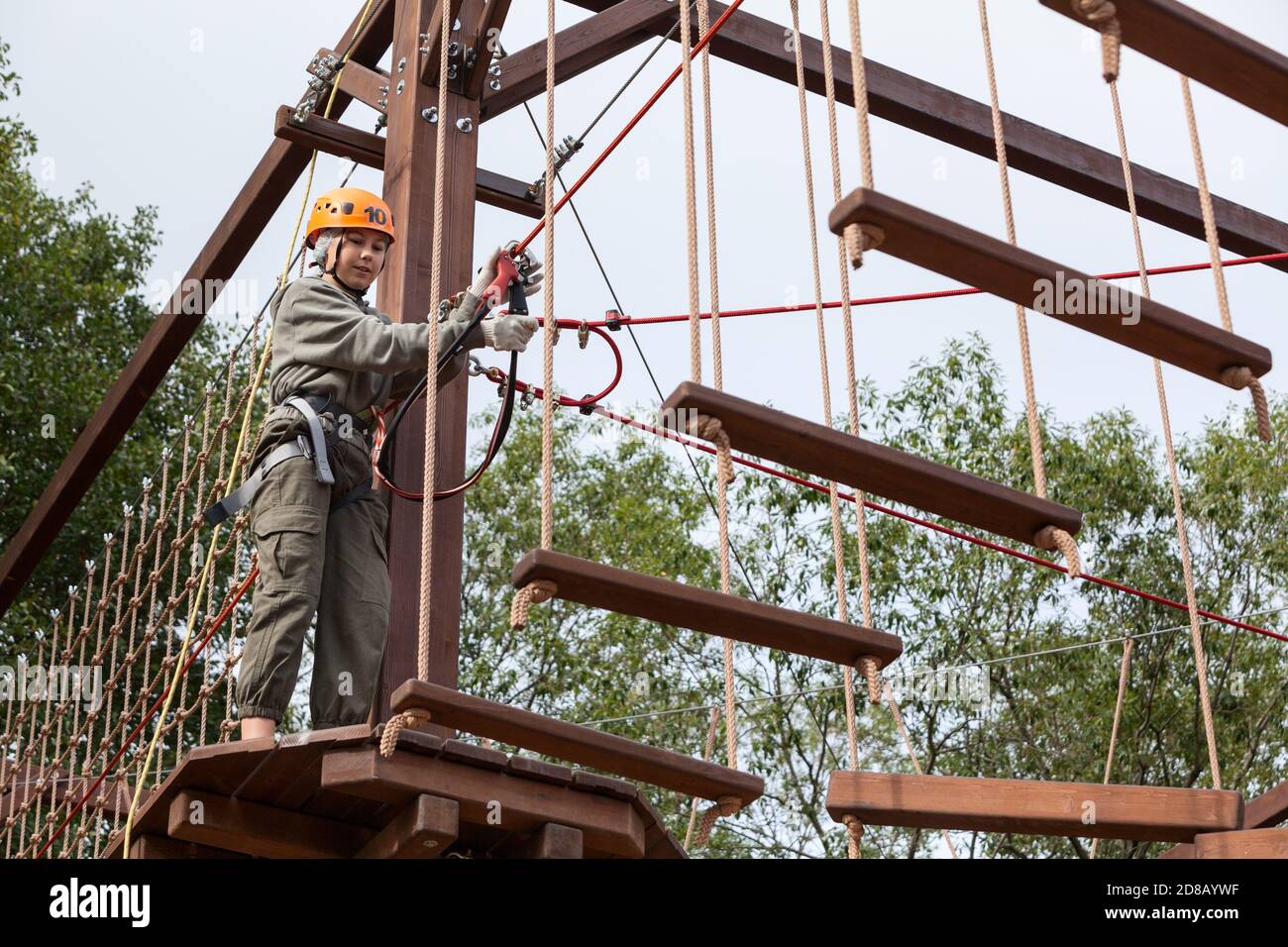 Teen girl on a rope course in a treetop adventure park passing hanging ropes obstacle Stock Photo