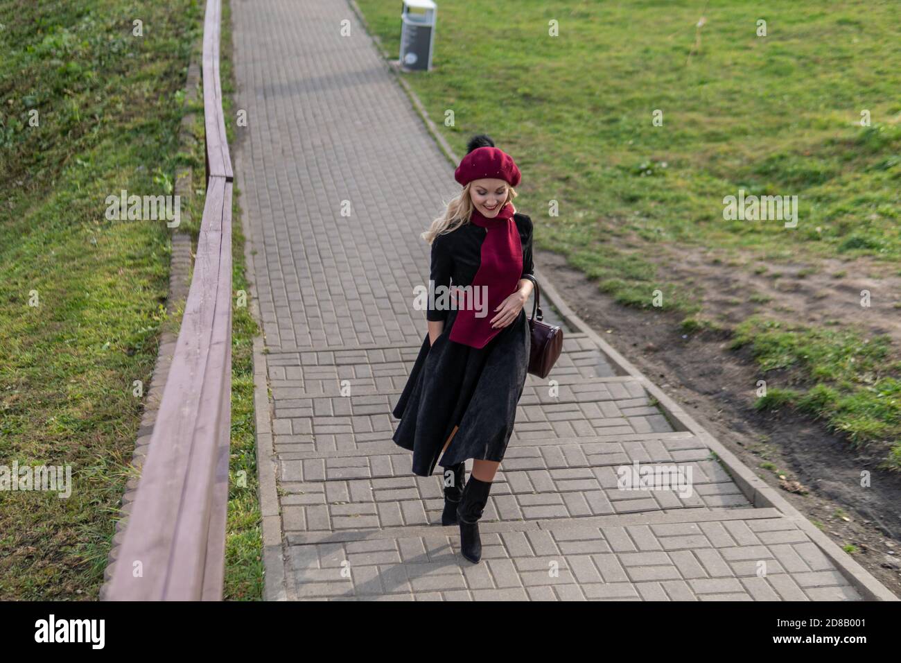 A joyful girl walks up the stairs in a burgundy palette and biret, with a beautiful smile in black clothes, in the fall against a background of blue Stock Photo