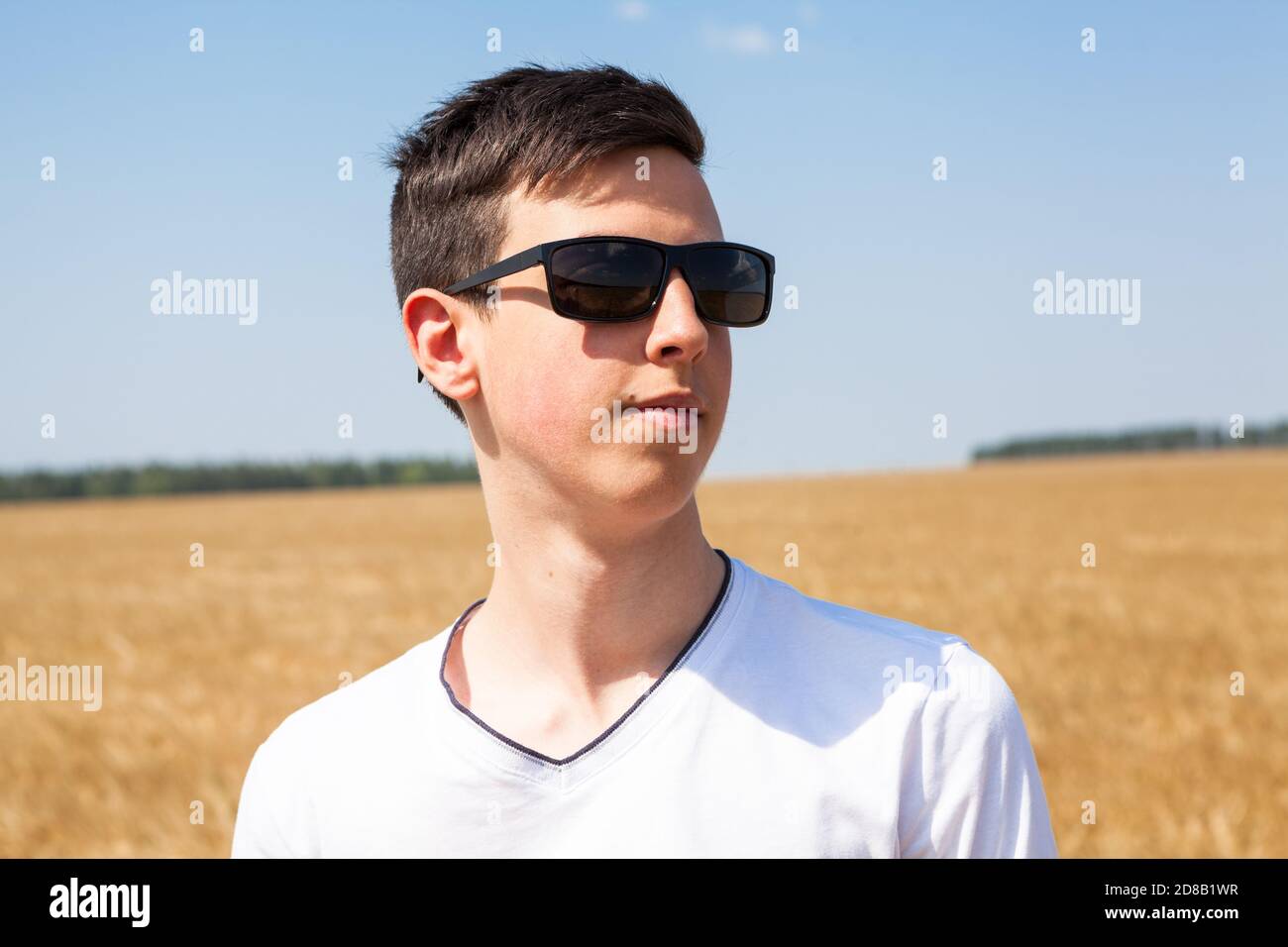 Teenage Caucasian boy portrait wearing black sunglasses, man standing on  wheat field at sunny day, white t-shirt Stock Photo - Alamy
