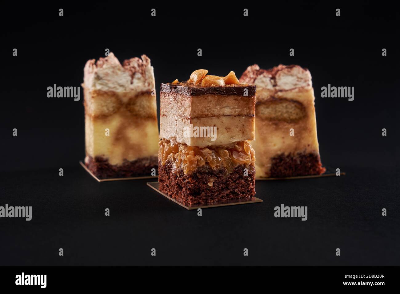 Tiramisu Cake With Three Layers Of Chocolate Biscuit And Natural Coffee Syrup With Cognac And Cream Three Square Pieces In Row Decorated With Whipped Cream And Cocoa Isolated On Black Background Stock