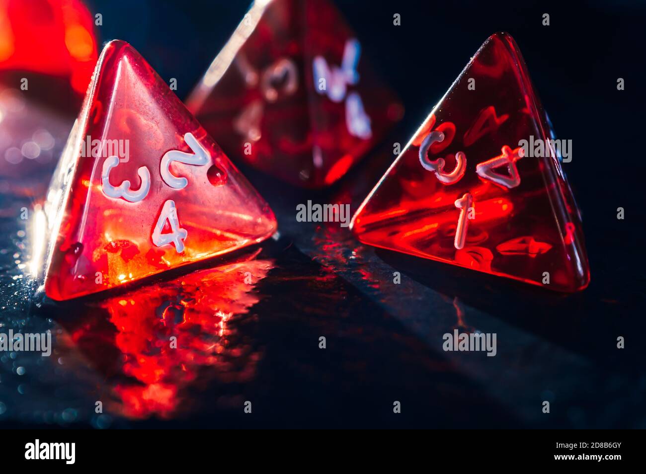 Close-up of four red transparent 4 sided dice on a wet slate surface. Focused on the foreground. Lens flare Stock Photo