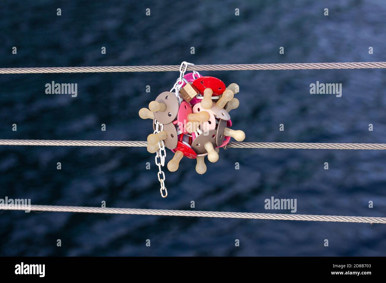 Bunch of baby pacifiers and a padlock fixed to a railing wire on a bridge. Hanging the dummies helps the toddler to get rid of them is a tradition in Stock Photo