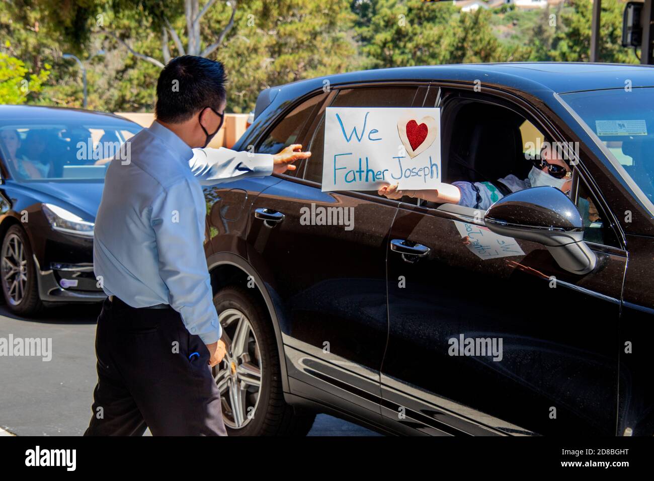 Drive through parishioners bid farewell to a departing priest Asian American at a Southern California Catholic church. Note face masks due to coronavi Stock Photo