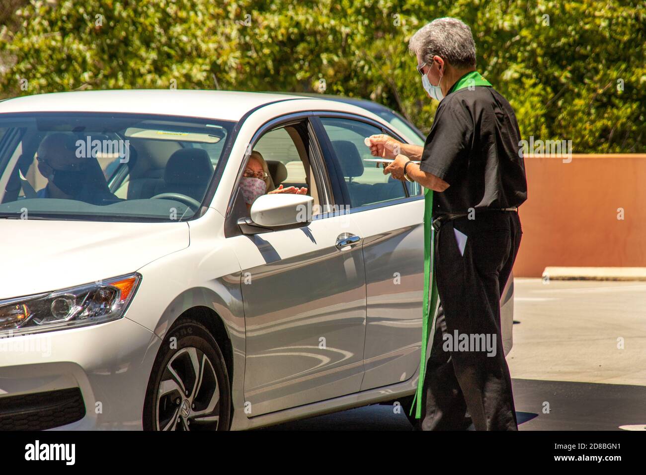 Wearing a face mask due to the coronavirus pandemic, the monsignor of a Southern California Catholic church offers drive through communion to his pari Stock Photo