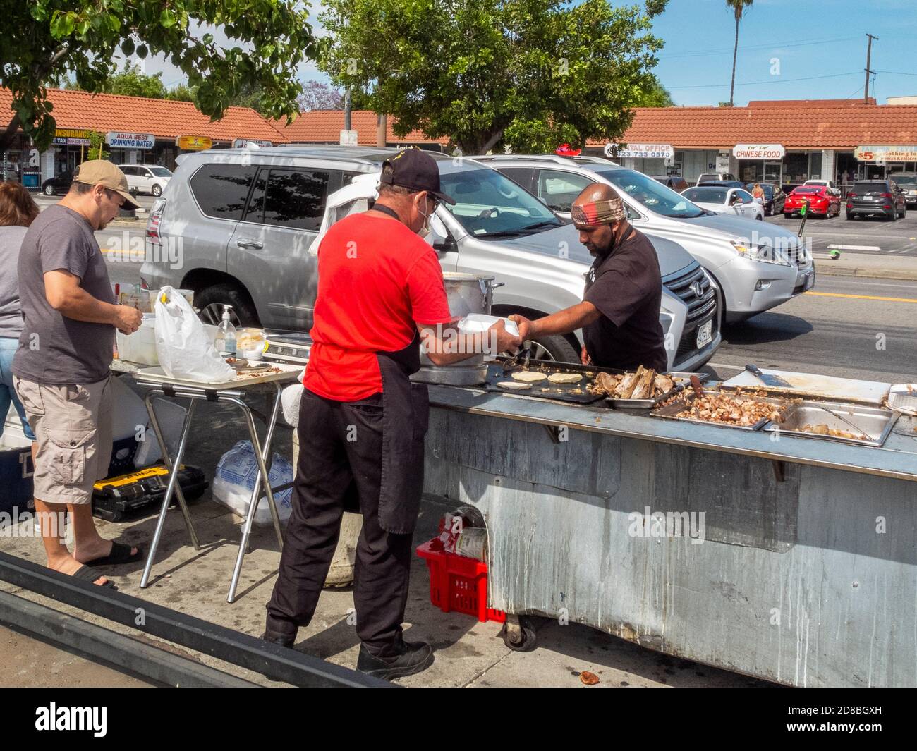 With restaurants closed in the coronavirus pandemic, an enterprising Hispanic chef moves his grill and pots outdoors to the sidewalk by a bus stop in Stock Photo