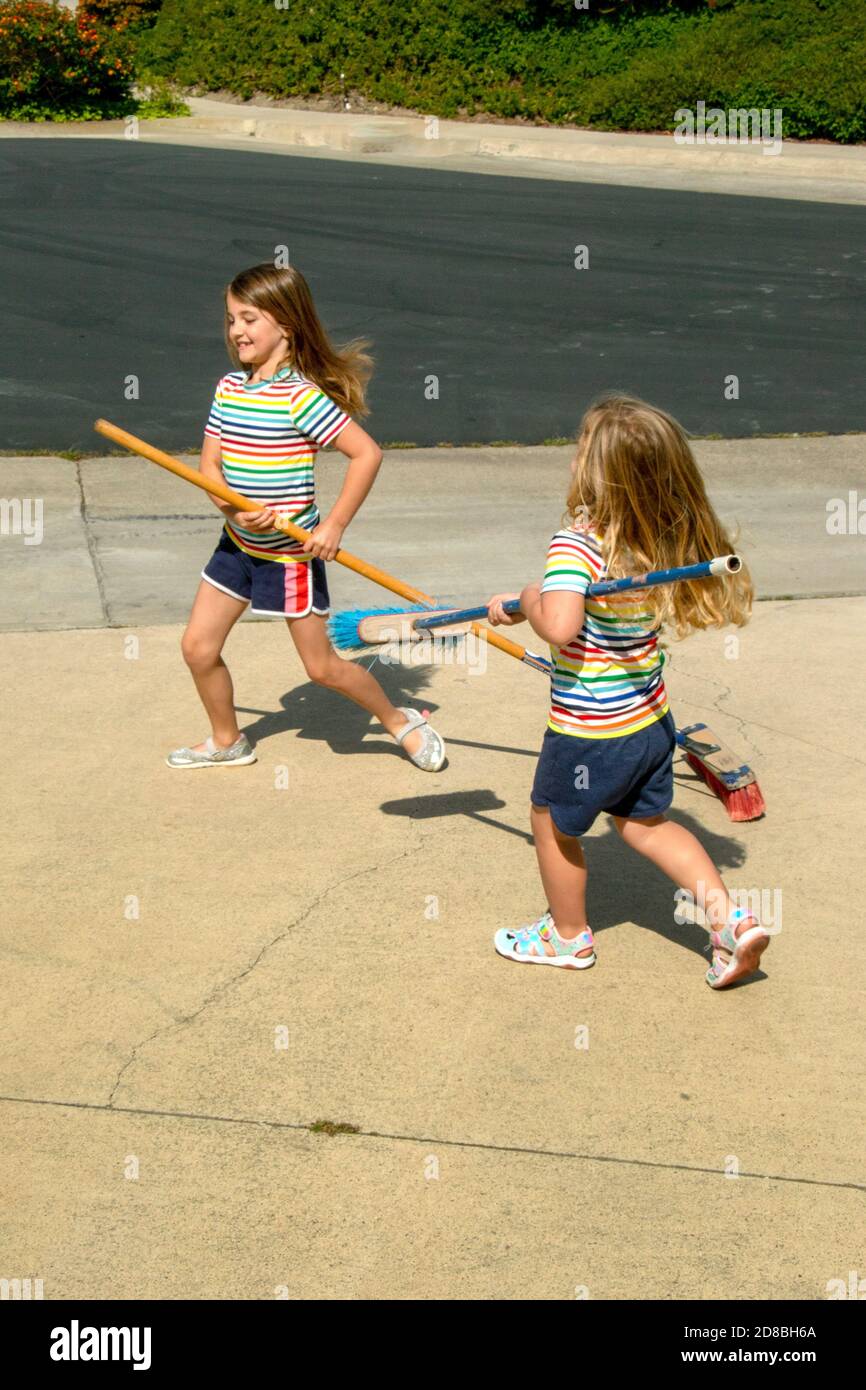 Identically dressed sisters sweep the driveway of their family home in suburban Laguna Niguel, CA. Stock Photo