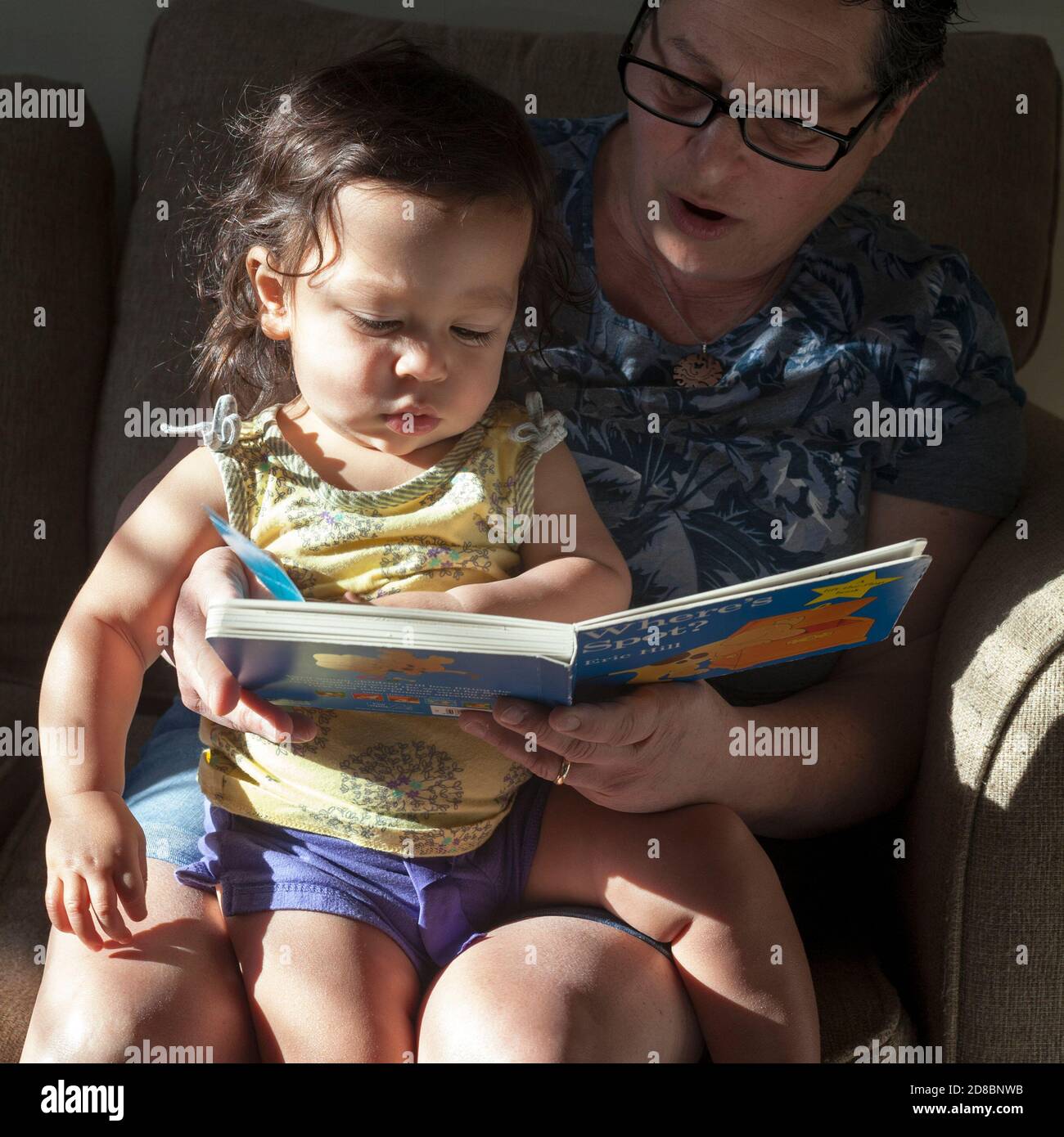 A one year old is read to by her grandmother. Stock Photo